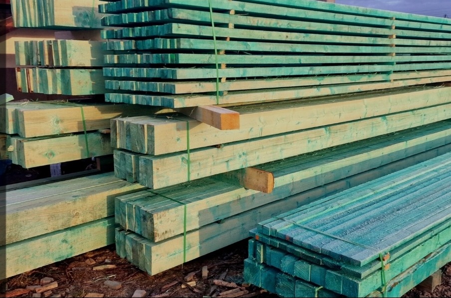 Stosy impregnowanych belek drewnianych, zabezpieczonych zielonym impregnatem i spiętych zieloną taśmą, przygotowane do budowy.
