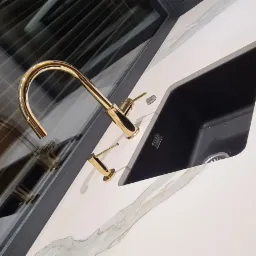 Biały blat kamienny z czarnym zlewem i złotą baterią, widoczne delikatne żyły na kamieniu, nowoczesny design.