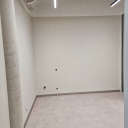 KG Koncept Kacper Gucz - Wnętrze biurowe po remoncie w Zamościu: gładkie, jasne ściany, surowy betonowy sufit z instalacjami, minimalistyczne oświetlenie. Przygotowane do dalszego wykończenia.