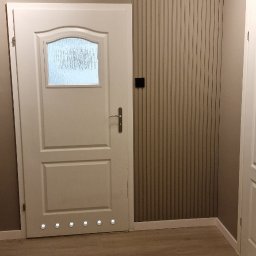 KG Koncept Kacper Gucz - Białe drzwi z szybą i podświetleniem LED u dołu, zamontowane w odnowionym wnętrzu z panelami ściennymi i drewnianą podłogą. Widok na fragment drugich drzwi.