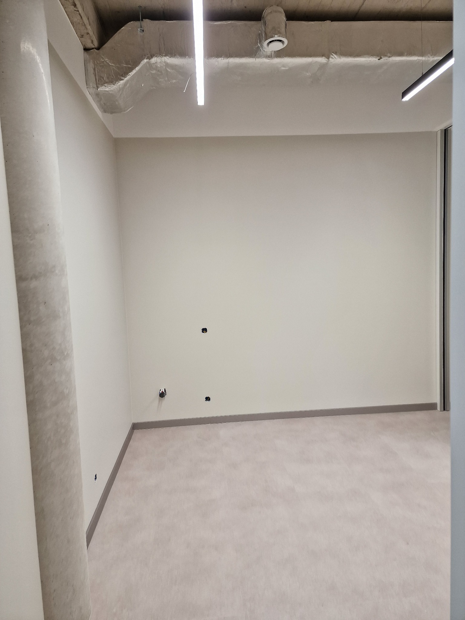 Wnętrze biurowe po remoncie w Zamościu: gładkie, jasne ściany, surowy betonowy sufit z instalacjami, minimalistyczne oświetlenie. Przygotowane do dalszego wykończenia.