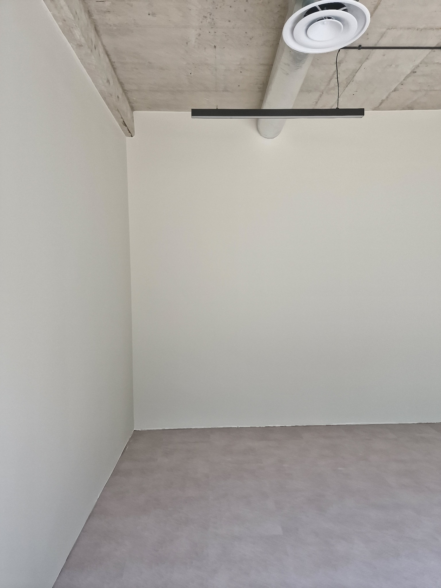 Jasne, świeżo pomalowane wnętrze z betonowym sufitem i nowoczesnym oświetleniem. Minimalistyczny design, gładkie ściany i podłoga w odcieniach szarości.