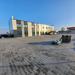 Nowoczesny budynek biurowy z płyt warstwowych w kolorach szarości i bieli, widok z zewnątrz, palety i resztki materiałów budowlanych na pierwszym planie.