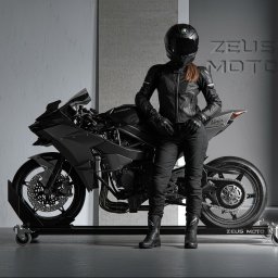 Sayna Polygons - Kobieta w czarnym kombinezonie motocyklowym i kasku stoi obok czarnego motocykla Kawasaki Ninja H2 na tle szarej ściany z logo Zeus Moto.