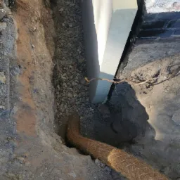 Fundament budynku z izolacją pionową, drenażem z otoczaków i rurą drenarską w geowłókninie, widok z góry na wykop.