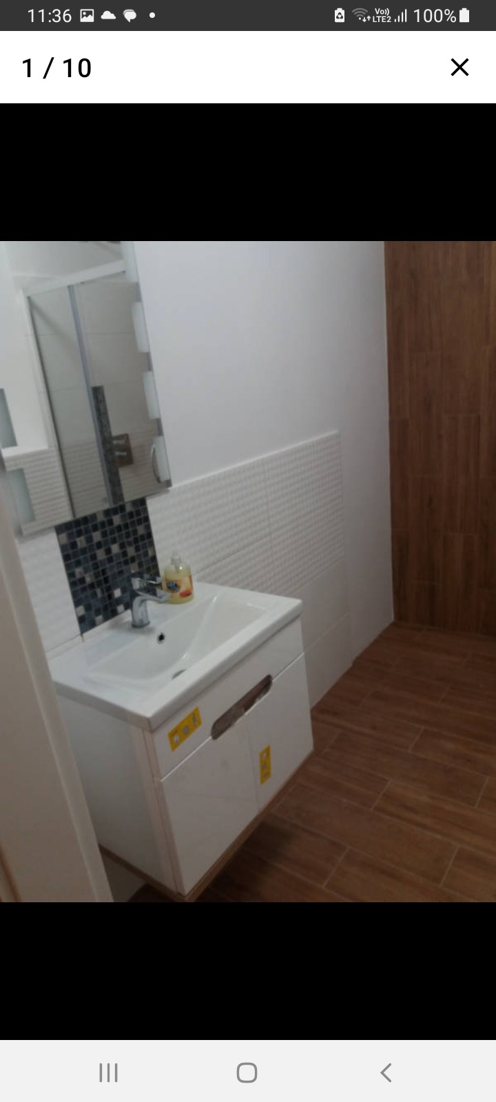 Nowoczesna umywalka nablatowa z szafką w łazience wykończonej białymi i mozaikowymi płytkami oraz drewnopodobną podłogą.