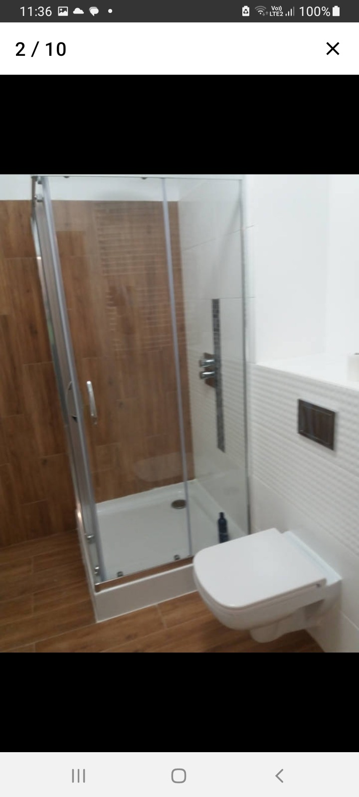 Nowoczesna łazienka z kabiną prysznicową z chromowanymi profilami i podwieszaną toaletą, wykończona płytkami imitującymi drewno i białymi płytkami strukturalnymi.