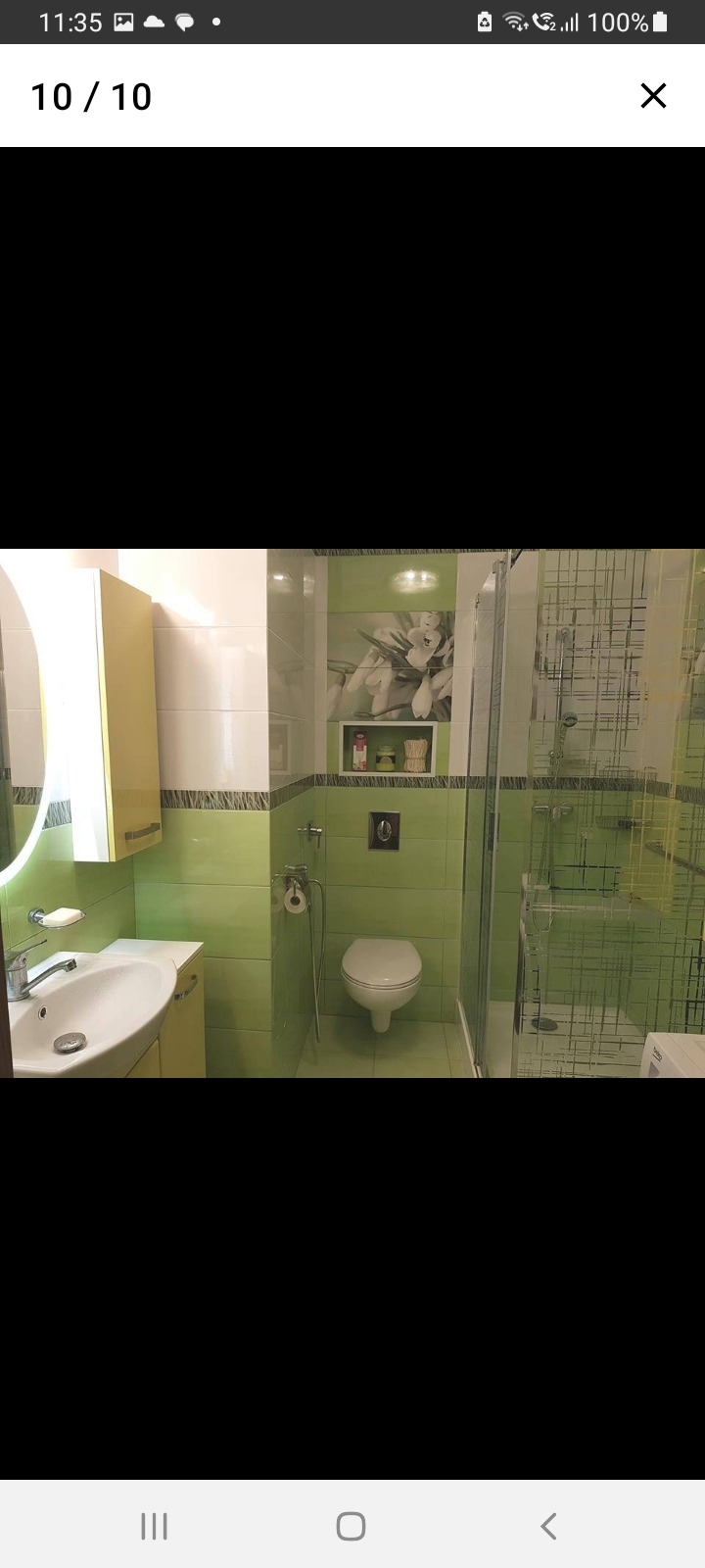 Jasnozielona łazienka z kabiną prysznicową, umywalką z szafką i toaletą; dekoracyjna grafika kwiatowa nad spłuczką.