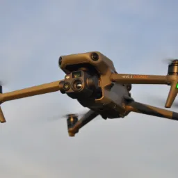 Latający dron Mavic 3 Enterprise z włączonymi zielonymi diodami LED na ramionach, na tle jasnego nieba.