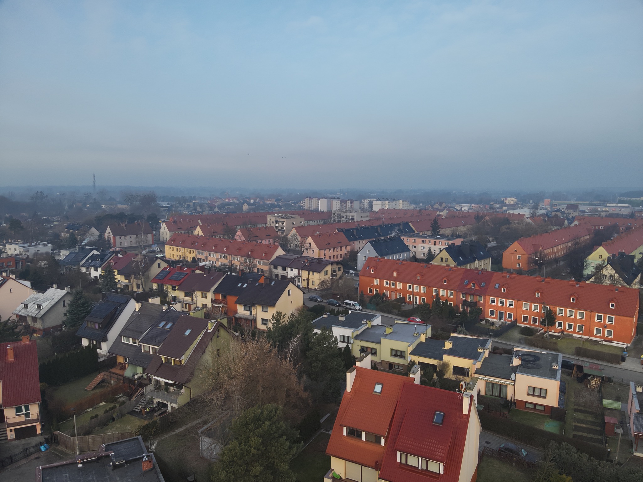 Panorama osiedla domów jednorodzinnych i szeregowych z czerwonymi dachami, widziana z góry w pochmurny dzień.