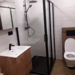 Nowoczesna łazienka z kabiną prysznicową z czarną ramą, umywalką z szafką w kolorze drewna i toaletą.