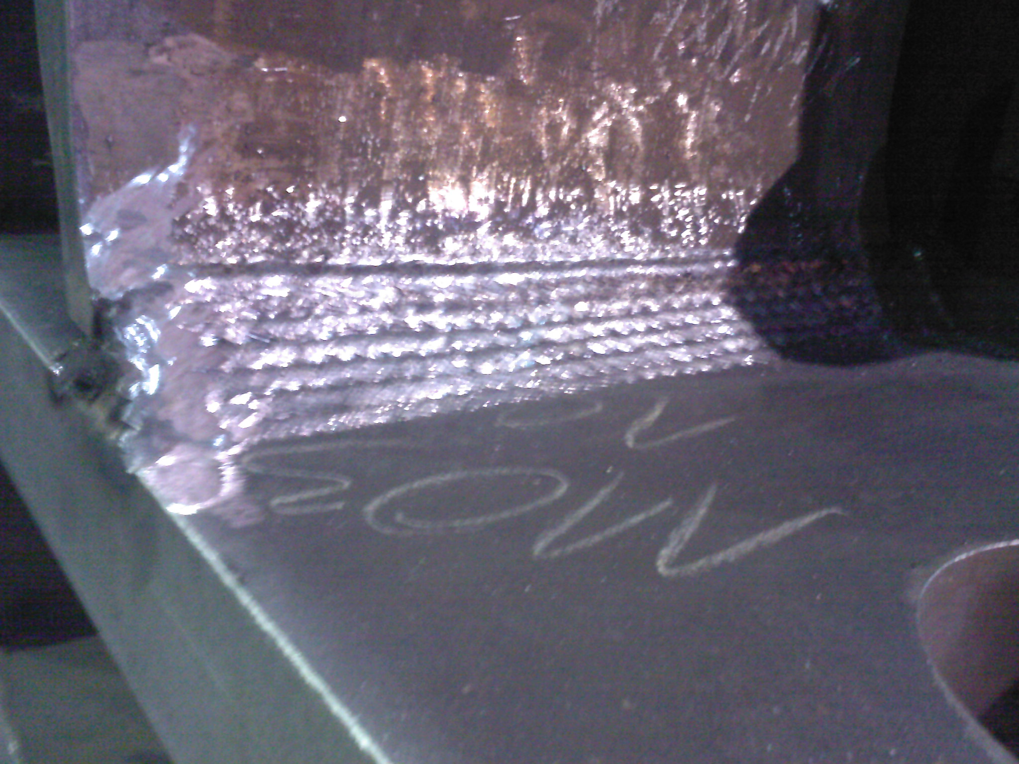 Detale spoiny na metalowym elemencie z widocznymi śladami po obróbce i napisem wykonanym kredą.