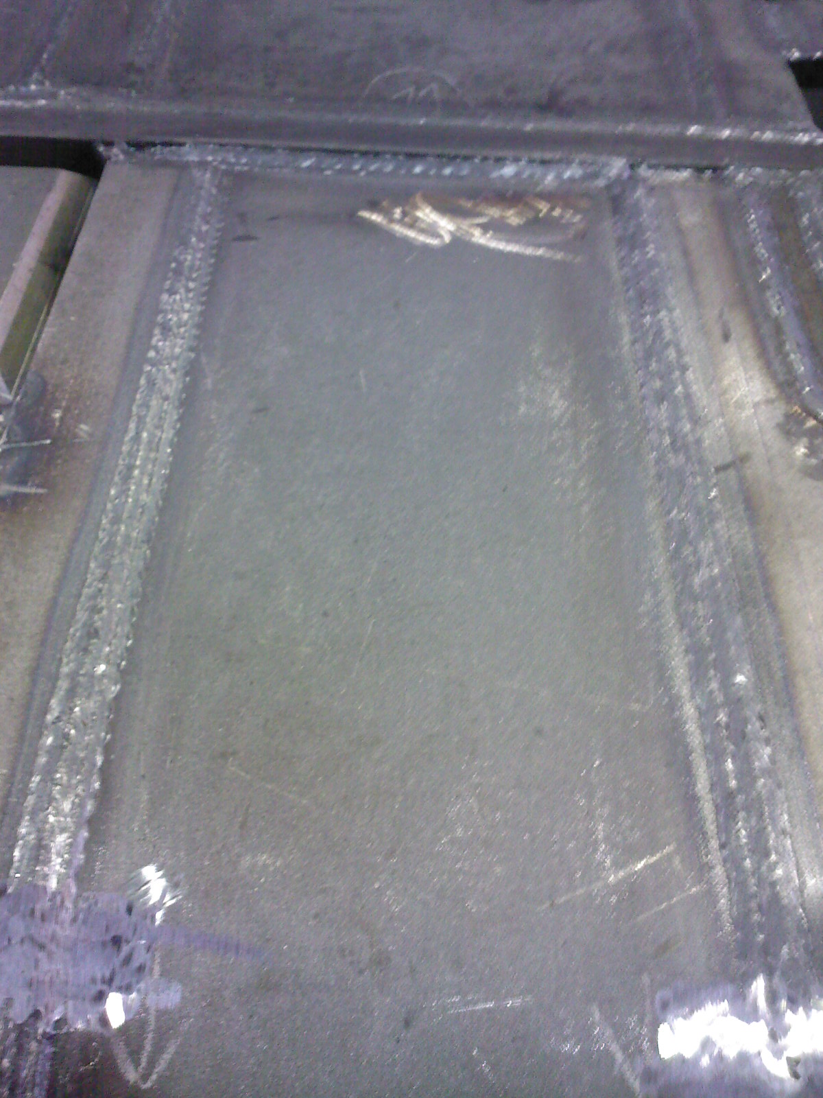 Szlifowana, stalowa powierzchnia po spawaniu z widocznymi śladami obróbki i spawami po bokach.