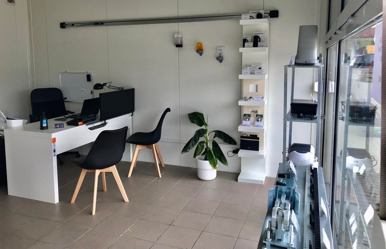 Wnętrze biura firmy oferującej automatykę do bram, z ekspozycją produktów na półkach i elementami bramy na pierwszym planie przy oknie.