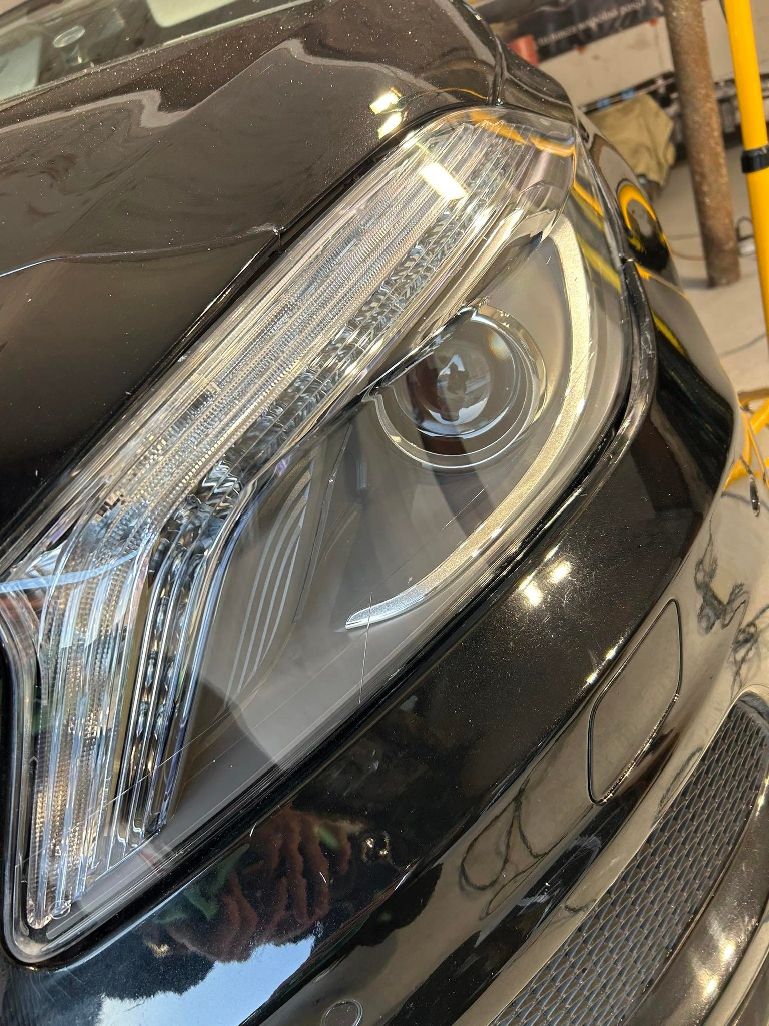 Szczegółowe ujęcie przedniego reflektora i fragmentu karoserii czarnego samochodu z widocznymi drobnymi zarysowaniami na lakierze.