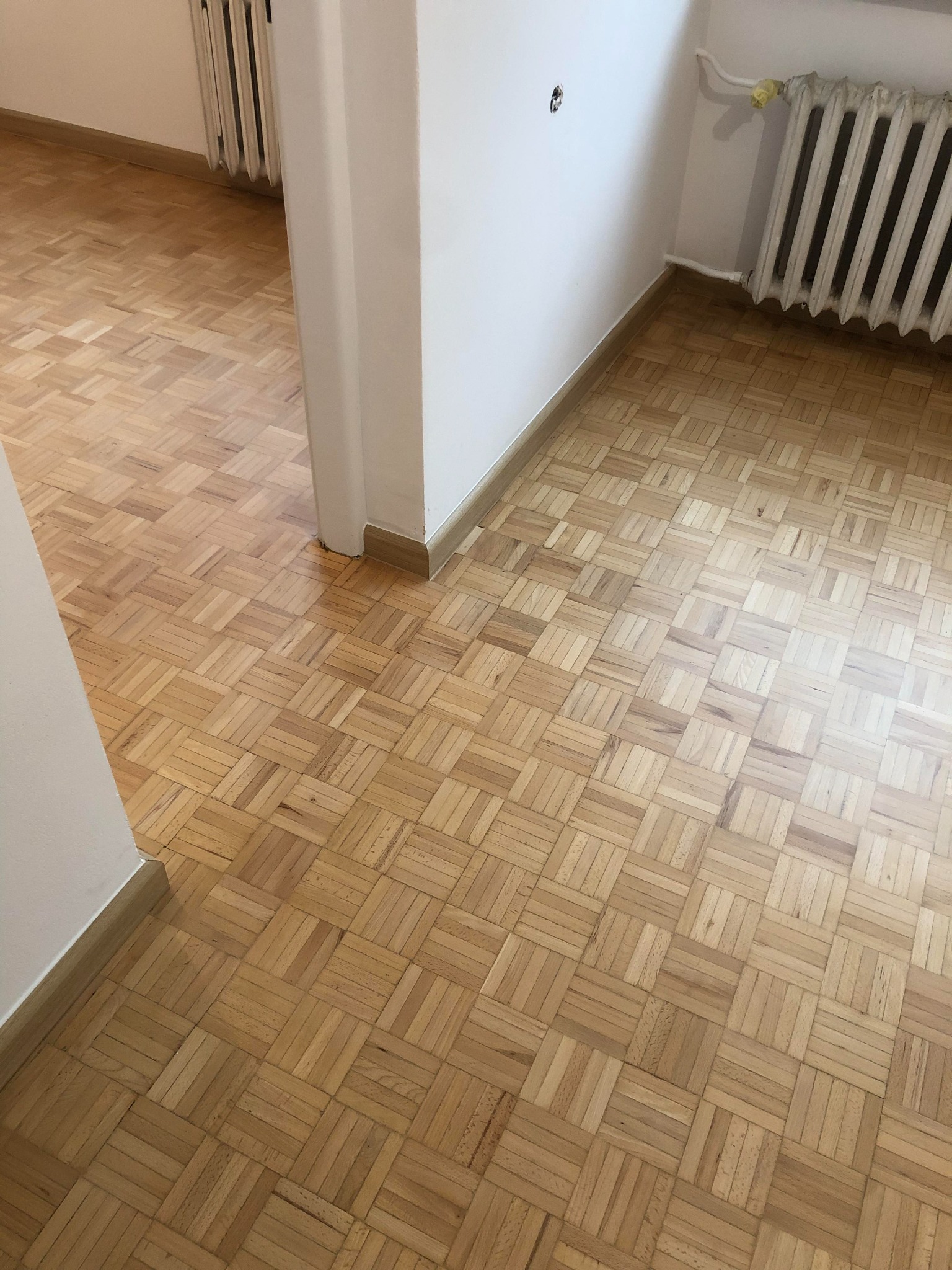 Parkiet ułożony w jodełkę francuską, widok z góry na fragment pokoju z grzejnikiem i białymi ścianami.