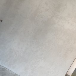 Bud-System - Świeżo wykończona ściana z efektem dekoracyjnym w odcieniach szarości i bieli, widoczna również szara podłoga z czerwoną taśmą wyznaczającą granice, oraz fragment instalacji wentylacyjnej pod sufitem.