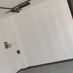 Bud-System - Puste pomieszczenie z szarymi płytkami podłogowymi pokrytymi śladami butów, białe ściany z widocznymi puszkami instalacyjnymi i czarnym systemem oświetlenia szynowego na suficie.