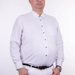 Portret mężczyzny w białej koszuli i spodniach na jasnym tle, wykonany w Bełchatowie, z widocznym zegarkiem na ręce i okularami z odblaskami.