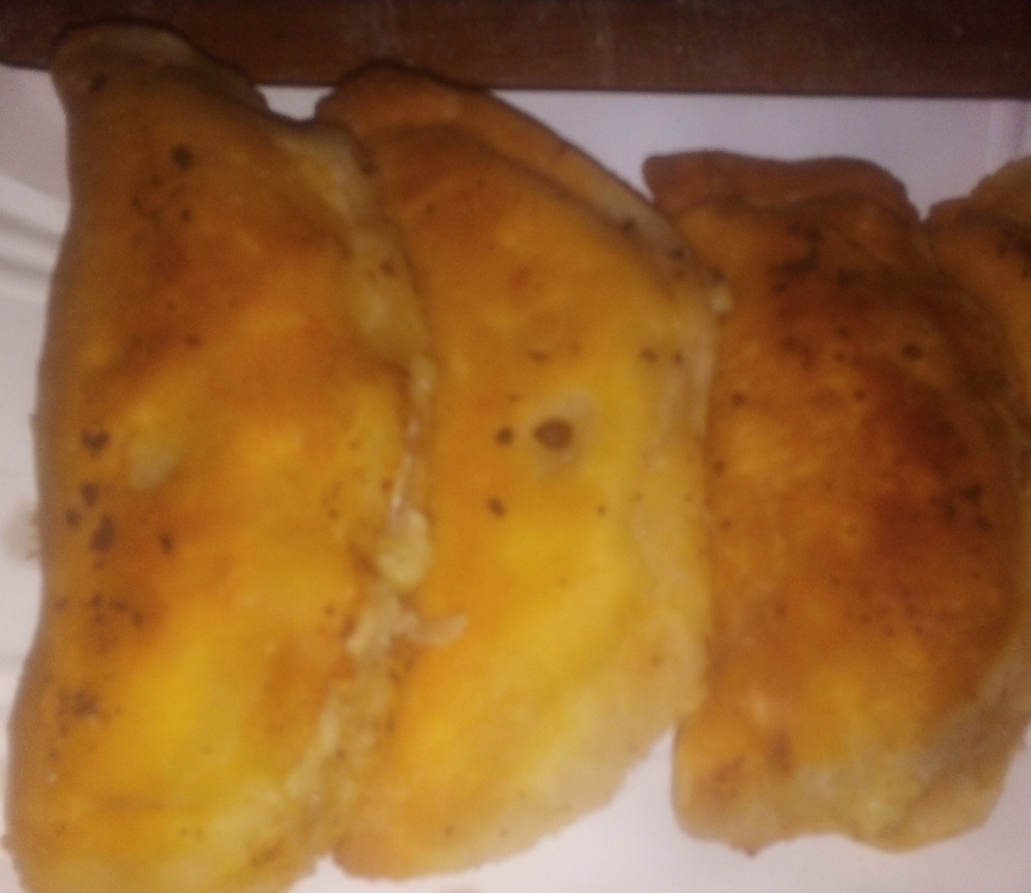 Ręcznie robione pierogi z mięsem, upieczone na złoty kolor, ułożone na białym talerzu, widoczne przyprawy na powierzchni.