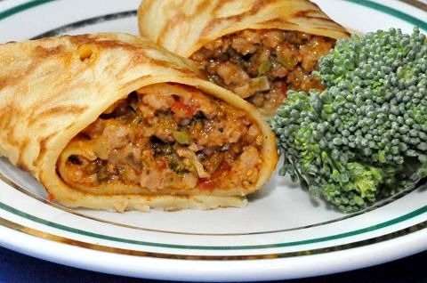 Dwa naleśniki faszerowane mięsem i warzywami, podane na talerzu z brokułem.