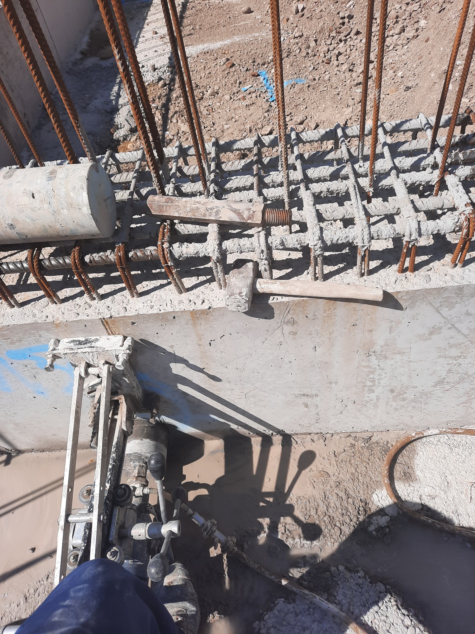 Zbrojenie pionowe i poziome zalane betonem, widoczny młotek, element wibrujący beton oraz fragment ubrania operatora wibrującego beton.