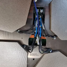 Wnętrze płyty indukcyjnej z widocznymi przewodami, złączkami i płytką drukowaną, widok z góry w trakcie podłączania.