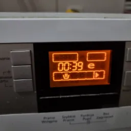 Wyświetlacz pralki z pomarańczowymi cyframi wskazującymi czas pozostały do końca cyklu, ustawienia prania wstępnego i szybkiego prania.