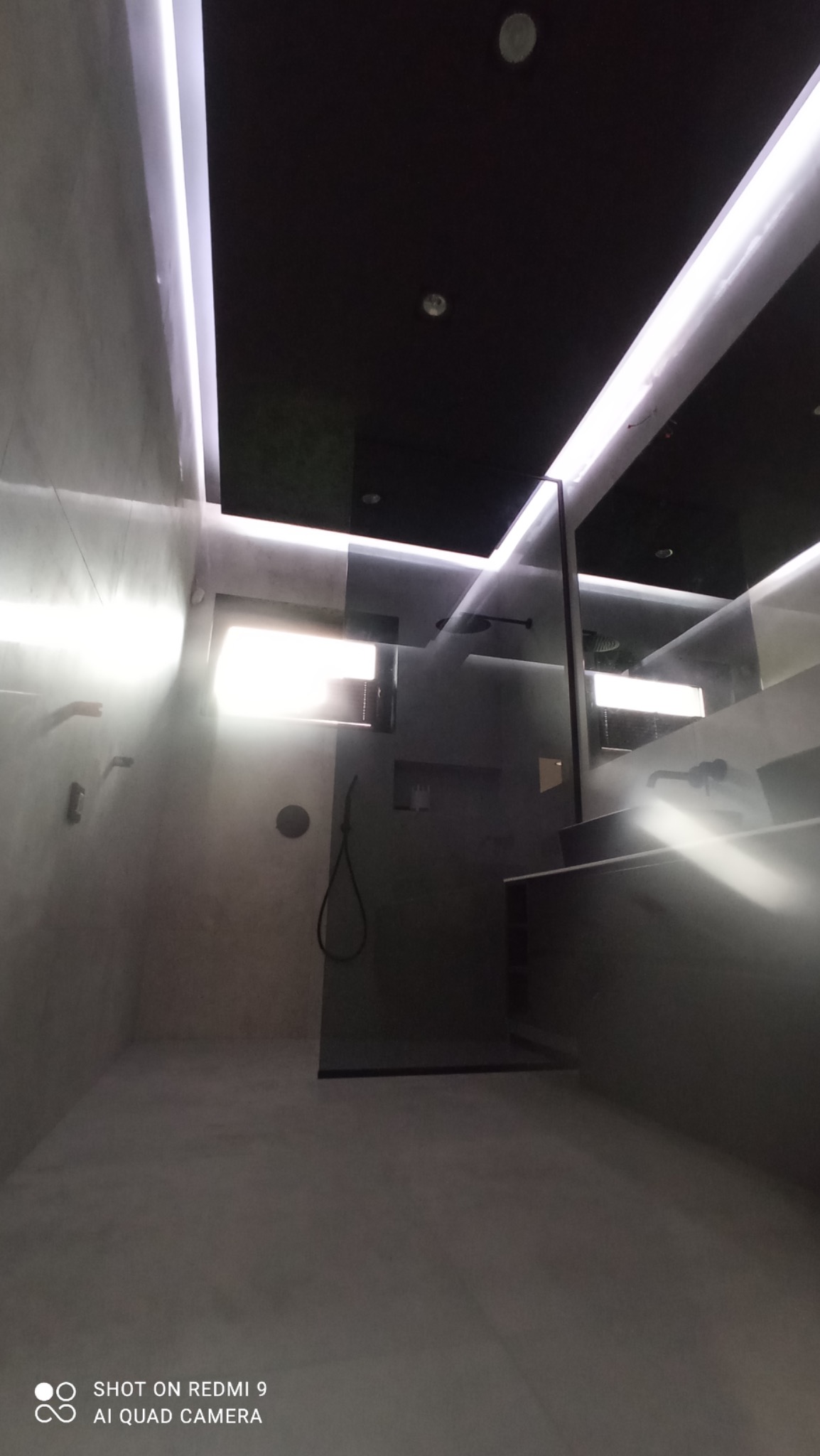 Nowoczesna łazienka w szarościach z podświetleniem LED w suficie i kabiną prysznicową typu walk-in.