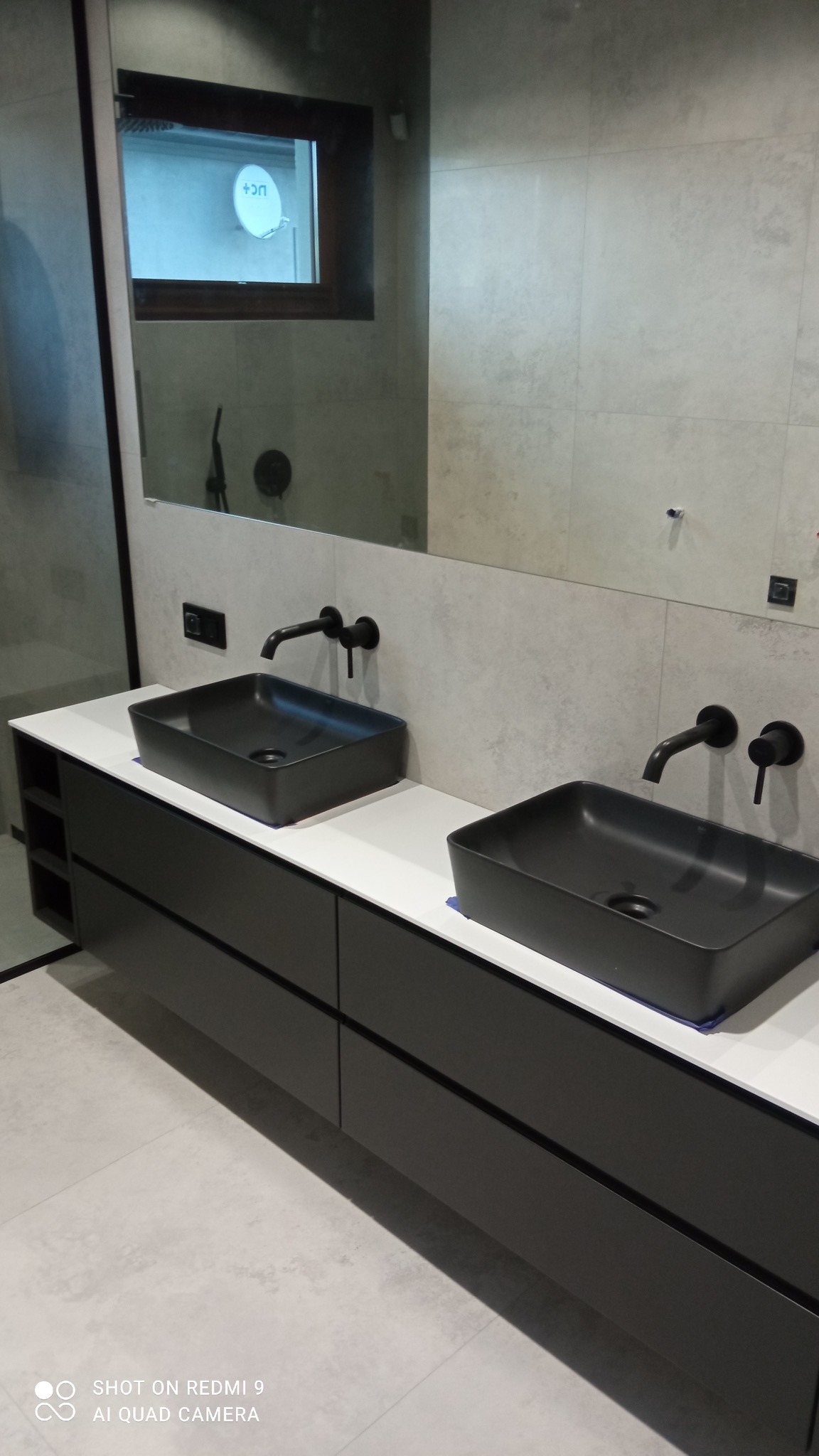 Nowoczesna łazienka z dwoma czarnymi, prostokątnymi umywalkami nablatowymi i minimalistyczną czarną armaturą na tle jasnoszarych płytek.