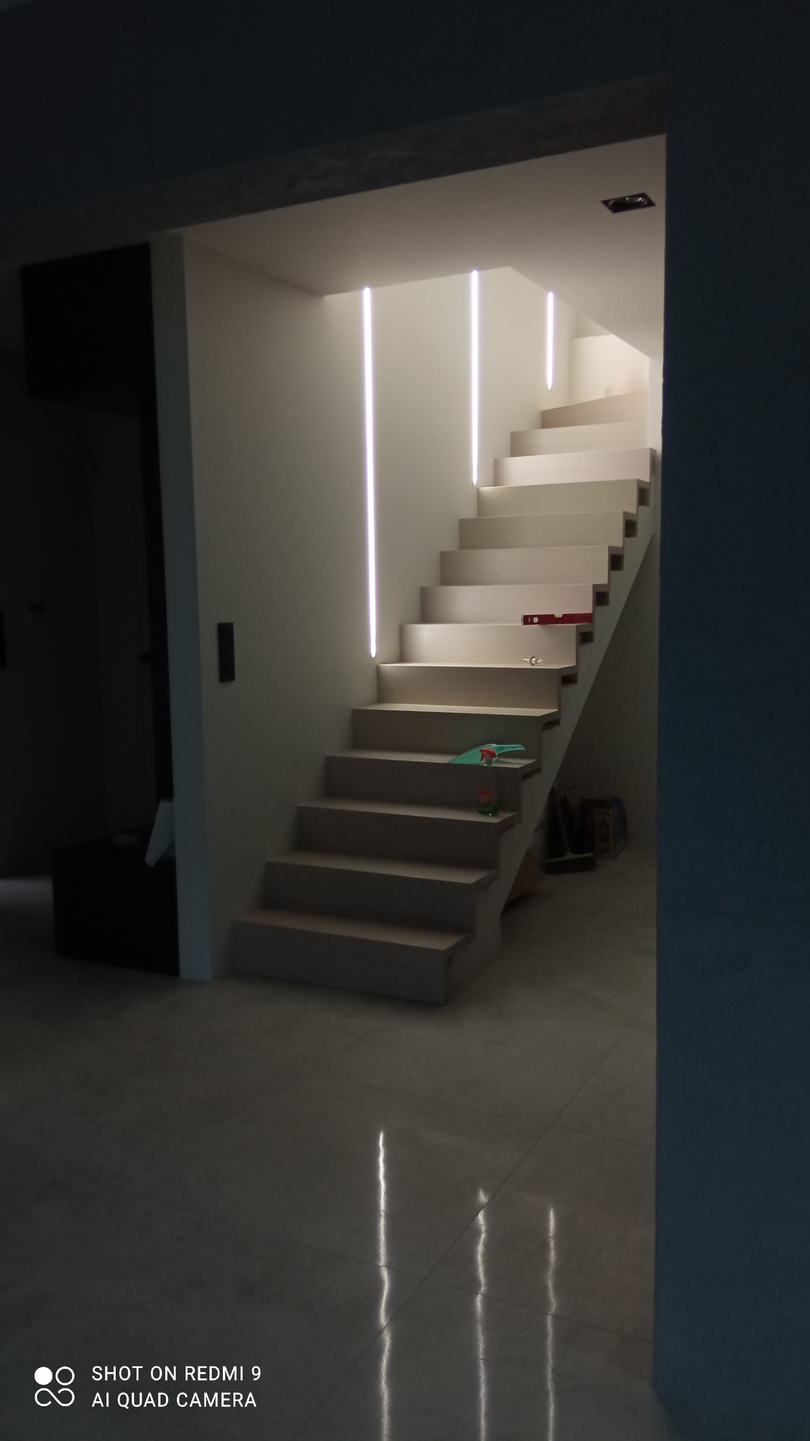 Nowoczesne schody wewnętrzne z podświetleniem LED, poziomica i butelka płynu do czyszczenia na stopniach.