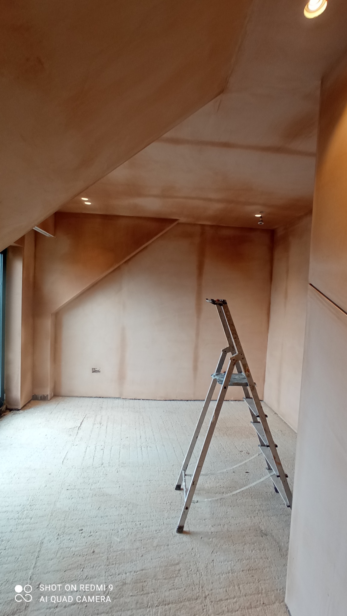 Pokój na poddaszu po nałożeniu wstępnej warstwy szpachli, widoczna drabina aluminiowa i wbudowane oświetlenie punktowe.