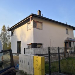 Move House Sp. Z o.o. - Dwukondygnacyjny dom z oknami zabezpieczonymi folią malarską, częściowo otynkowany, z czarną stolarką i dachem. Widoczne skrzynki gazowe i auto.