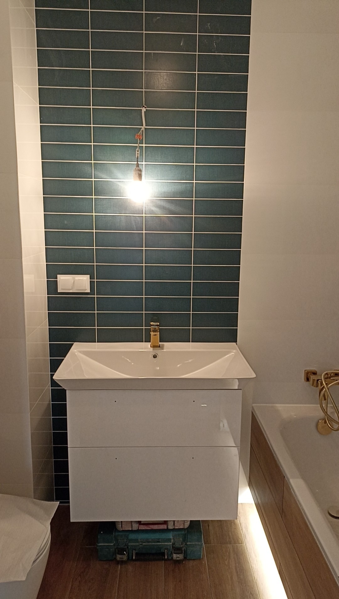 Nowoczesna łazienka w trakcie wykańczania: biała szafka z umywalką, ciemnozielone płytki na ścianie, widoczna skrzynka z narzędziami.