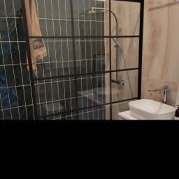 Budownictwo Komercyjne Grzegorz Bierecki - Nowoczesna łazienka z kabiną prysznicową typu walk-in z czarnymi profilami, umywalką nablatową i baterią w minimalistycznym stylu, na ścianach płytki w odcieniach zieleni i beżu.