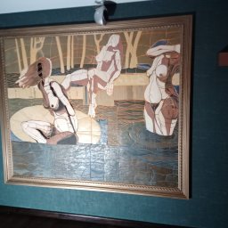 NOTO FLIZ - Mozaika ceramiczna przedstawiająca trzy postacie kobiece w abstrakcyjnym otoczeniu, oprawiona w złotą ramę, zamontowana na ciemnozielonej ścianie z fakturą.