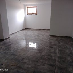 NOTO FLIZ - Surowe, ciemne płytki podłogowe w pustym pomieszczeniu z świeżo pomalowanymi na biało ścianami i małym oknem w drewnianej ramie.