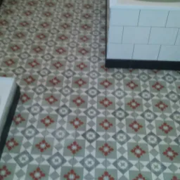 Wzorzysta, nowa podłoga z płytek w łazience, z widoczną wanną obłożoną białymi kafelkami i fragmentem umywalki.