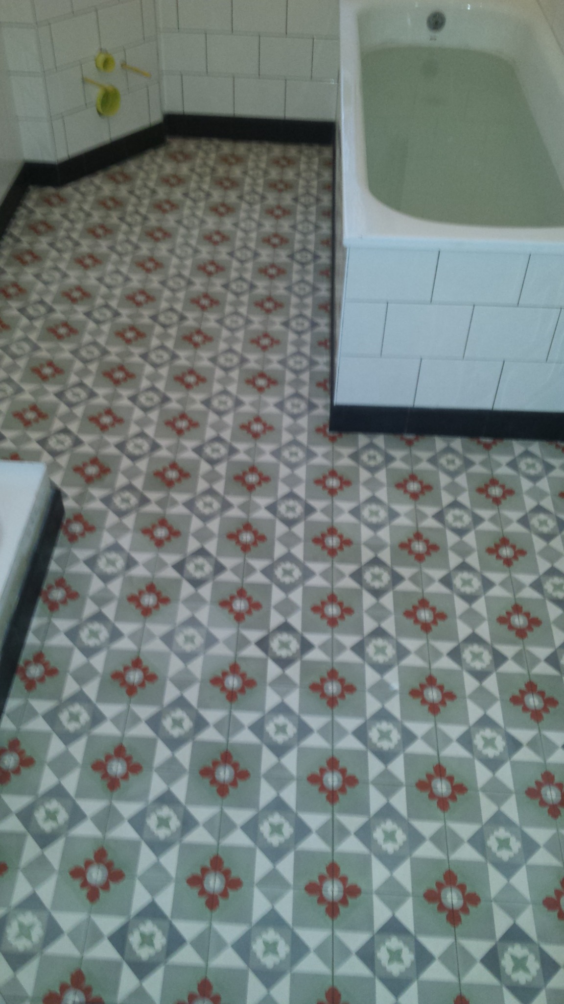 Wzorzysta, nowa podłoga z płytek w łazience, z widoczną wanną obłożoną białymi kafelkami i fragmentem umywalki.