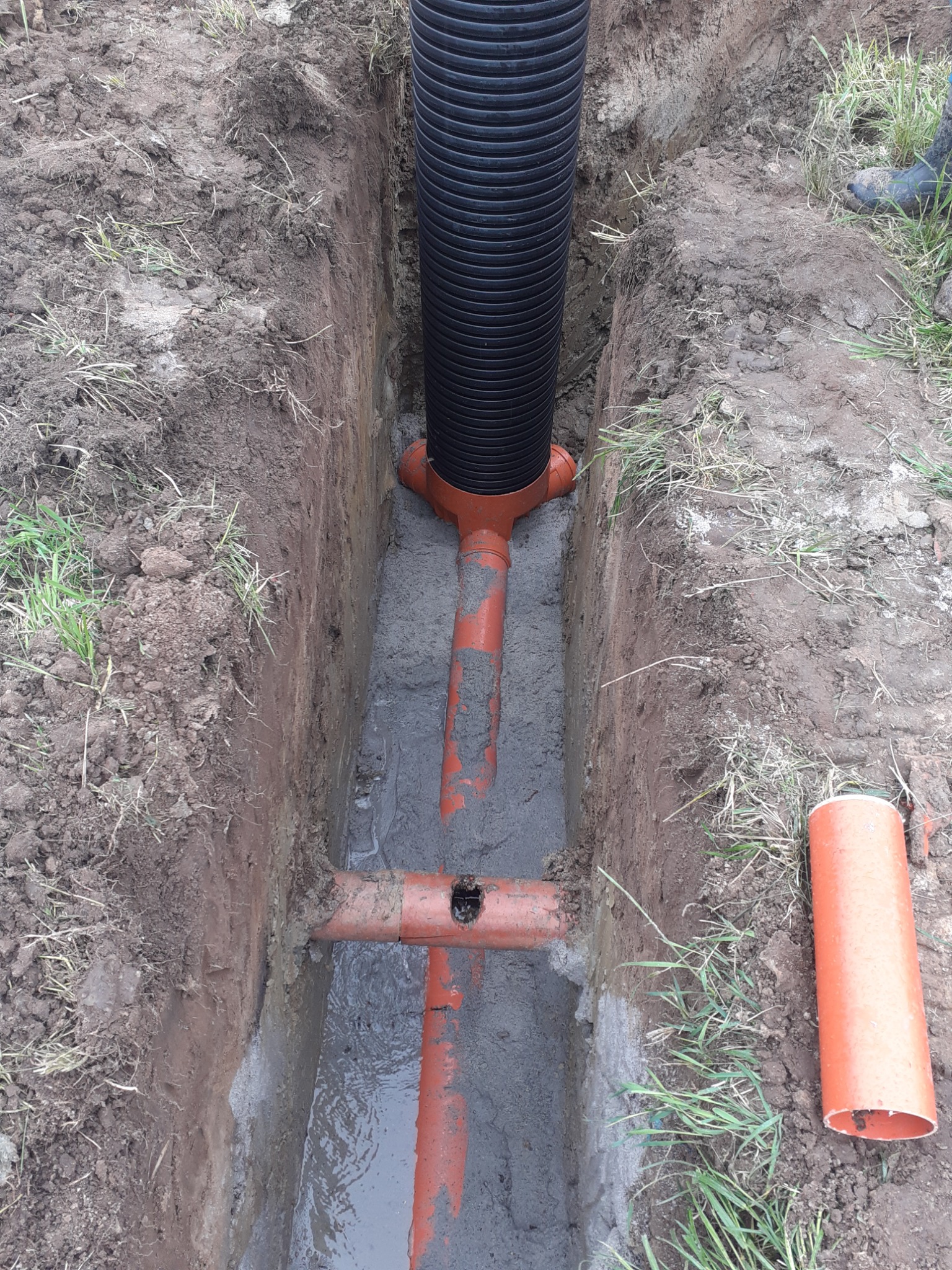 Wykop w ziemi z ułożonym systemem rur drenarskich z tworzywa sztucznego, częściowo zalany wodą, widok z góry.