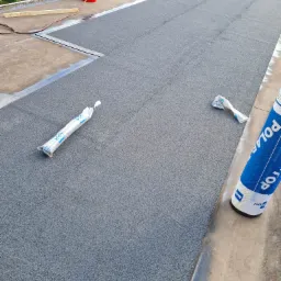 Szary, płaski dach pokryty papą termozgrzewalną, widoczna butla gazowa Cagogas, rolka papy Polar Top oraz dwa opakowania papy w folii.