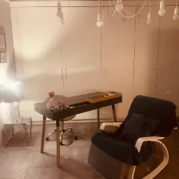 Pokój terapeutyczny z czarnym biurkiem, klepsydrą, lampą na stoliku i wygodnym fotelem bujanym pod wiszącą lampą z żarówek.