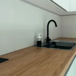 Drewniany blat kuchenny z czarnym, minimalistycznym kranem i dozownikiem mydła w przezroczystej butelce z czarną zawartością, widok z niskiego kąta.