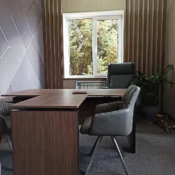 Nowoczesne biuro z biurkiem w kształcie litery L z ciemnego drewna, krzesłami na metalowych nogach i dużym oknem z widokiem na drzewa, dekoracyjne panele ścienne w odcieniach szarości i brązu.