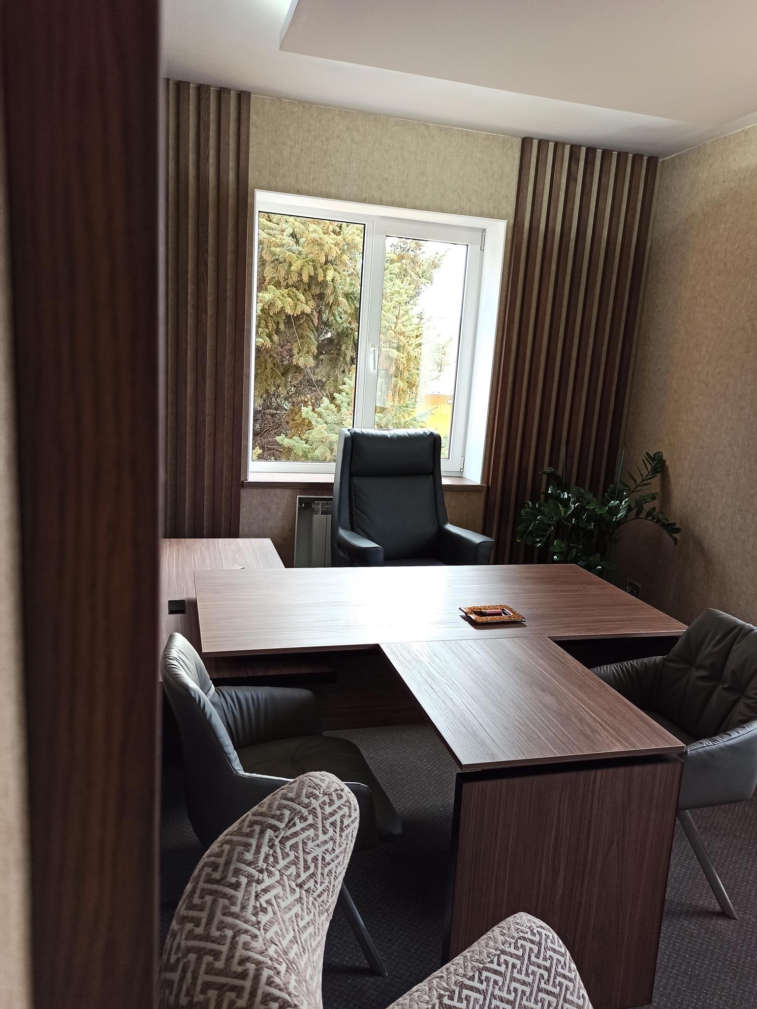 Nowoczesne biuro z dużym, narożnym biurkiem z drewnianym blatem, skórzanym fotelem i dekoracyjnymi lamelami ściennymi w kolorze drewna.