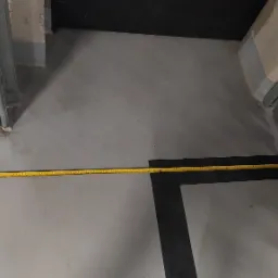 Pomiar długości w garażu przy użyciu żółtej taśmy mierniczej; widoczny fragment bramy garażowej i metalowa konstrukcja ścian.