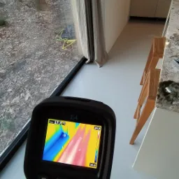 Pomiar termowizyjny okna w nowoczesnym domu, widoczny termogram na ekranie kamery Flir E4, wskazujący na rozkład temperatur w okolicy ramy okiennej.