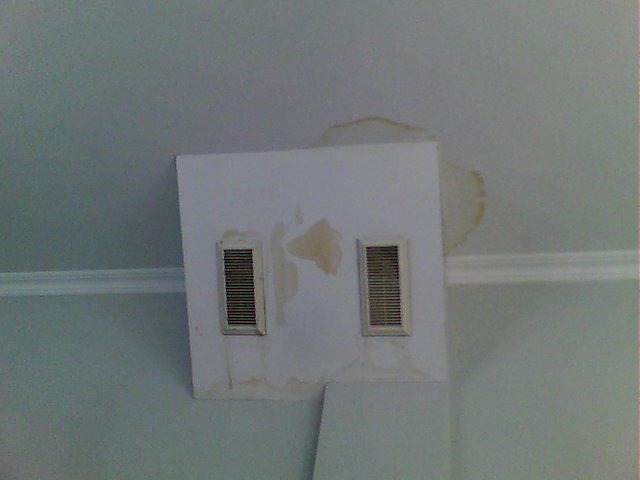 Fragment sufitu z widocznymi plamami po przecieku i osadzonymi kratkami wentylacyjnymi, ślady wilgoci wokół kratek.