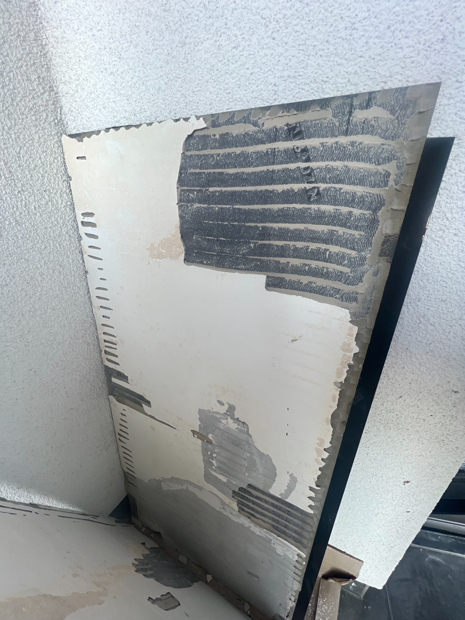 Uszkodzona płyta sufitowa z widocznymi śladami kleju i nierównościami, częściowo oderwana od sufitu podwieszanego.