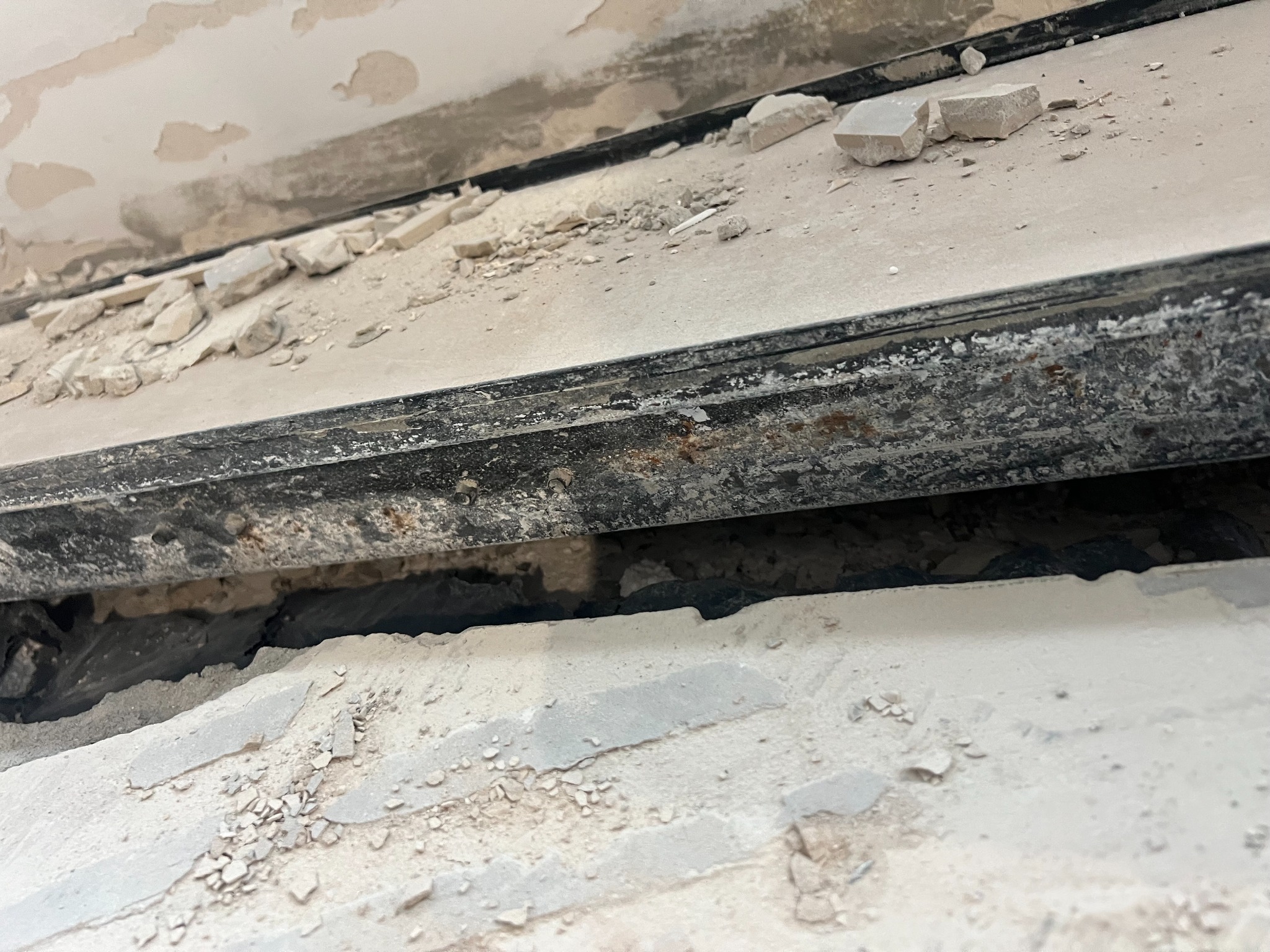 Fragment uszkodzonego stropu z widocznymi elementami konstrukcyjnymi i gruzem, ukazujący zakres prac naprawczych lub inspekcji budowlanej.